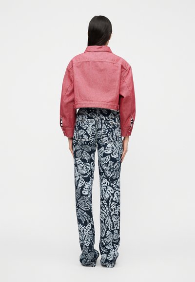 Veste en denim rouge raccourcie avec un col pointu, et pantalon bleu à motifs avec des textes graphiques blancs et des dessins de feuilles.