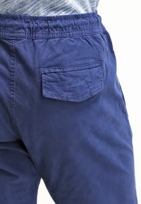 Námořnické modré kalhoty s texturovaným povrchem, vybavené elastickým pasem a zadní kapsou s zakřiveným prošíváním.