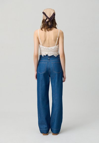 Top court en dentelle blanche avec bretelles ajustables, associé à un jean en denim bleu taille haute et jambes larges. L'ensemble présente une coupe décontractée.