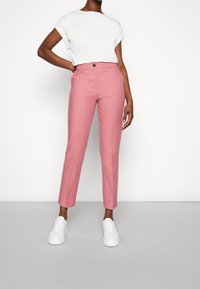 Rosa skräddarsydda byxor med rak passform, två fickor och en enkel knappstängning, kombinerat med en vit topp med kort ärm och vita sneakers.