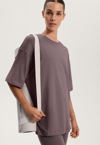 Volná, krátkosrstá, mauve tričko v kombinaci s bílou síťovou taškou. Hladký materiál a uvolněný design, vhodné na každodenní nošení nebo cvičení.