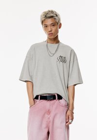 T-shirt oversized grigio chiaro con una grafica nera sul petto, abbinata a jeans in denim rosa sbiadito e una cintura nera.