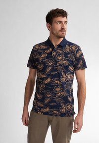 Marinblå polo med blommönster i guldtoner, kort ärm och fast krage. Strukturerad tyg och figursydd passform för komfort.