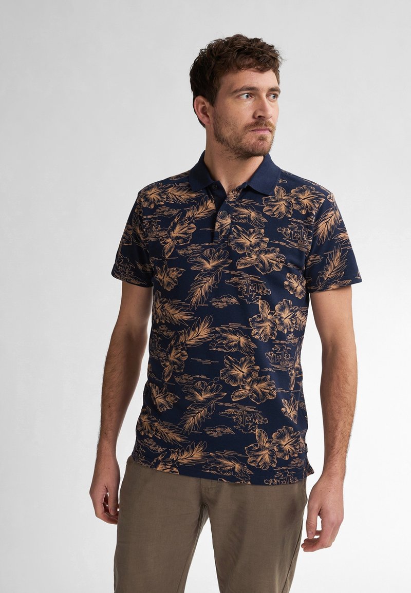 Marinblå polo med blommönster i guldtoner, kort ärm och fast krage. Strukturerad tyg och figursydd passform för komfort.