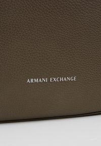Pelle marrone testurizzata con logo in rilievo "ARMANI EXCHANGE" in bianco. La superficie presenta una fine trama, che ne esalta l'aspetto di alta qualità.