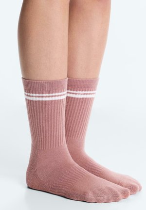 Legs wearing ribbed pink socks with two white stripes near the top, standing on a white surface with a light background.