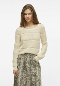 Lichtbeige gebreide trui met gestructureerde strepen en ribbelmanchetten, gecombineerd met een grijze rok met slangenprint die een knoopsluiting en zakken heeft.