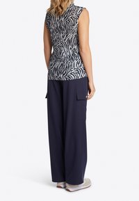 Top bez rękawów w czarno-biały wzór zebry, w parze z luźnymi, granatowymi spodniami cargo z bocznymi kieszeniami i swobodnym krojem.