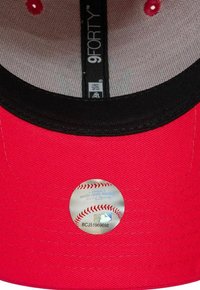 Gorra de béisbol roja con visera negra, que presenta un adhesivo reflectante en el interior con un diseño de béisbol y detalles de texto.