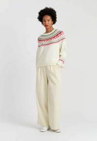 Cream sweater with multicolor geometric patterns at the neckline, paired with wide-leg beige trousers and white sneakers.