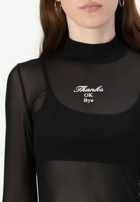 Black sheer long-sleeve top with high neck; features white text: “Thanks OK Bye.” Text is centrally placed on the chest area.
