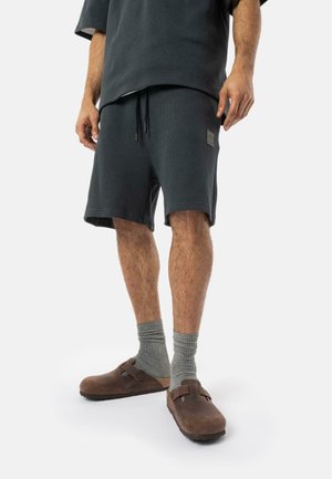 Ensemble en tricot texturé gris foncé comprenant un haut à manches courtes ample et un short assorti, complété par des chaussettes grises et des sabots marron.