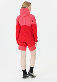 Röd och rosa jacka med huva, matchande röda shorts och svarta strumpor i kombination med vandringsskor. Slätt tyg och sportig design.