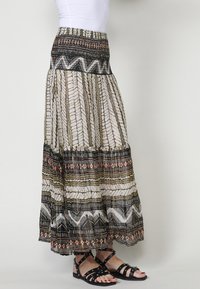 Maxi-rok van lichtgewicht stof met meerkleurige geometrische patronen, voorzien van een smock-elastische tailleband en een gelaagde zoom. Zwarte sandalen zichtbaar.