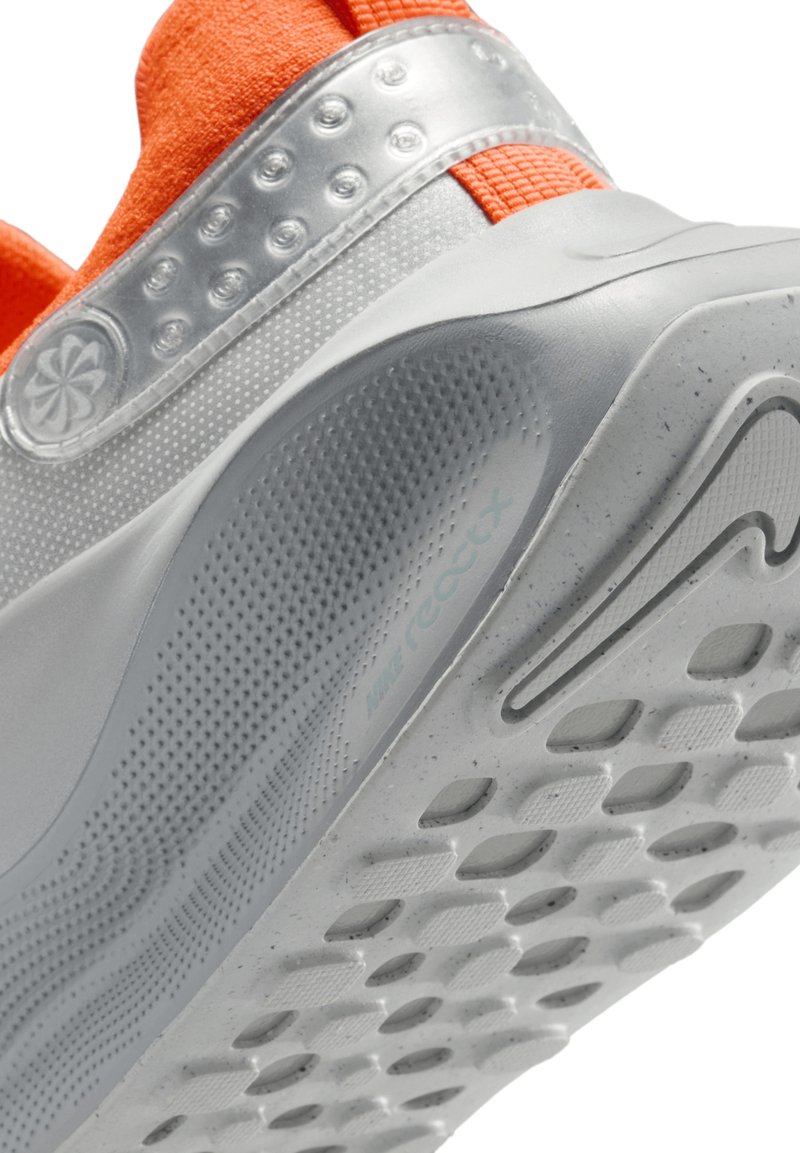 Białe buty sportowe z szarym siatkowym wierzchem, pomarańczowymi akcentami i wzorzystą podeszwą. Posiadają teksturowany obcas i elastyczną gumową podeszwę.