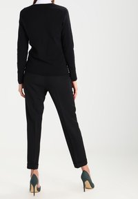 Schwarzer, langärmeliger Pullover mit rundem Ausschnitt, kombiniert mit schwarzen Hosen, mit Bündchen und grünen High Heels mit beiger Sohle.