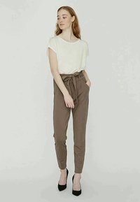 White short-sleeve t-shirt paired with high-waisted, tailored brown trousers featuring a tied belt. Worn with black high-heeled shoes.