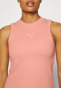 Jasnoróżowa, bezrękawnikowa top sportowy z teksturowanej tkaniny; posiada małe białe logo Pumy na obszarze klatki piersiowej.