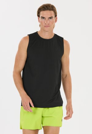 Man wearing a sleeveless black sports shirt and bright yellow-green shorts standing against a plain white background.