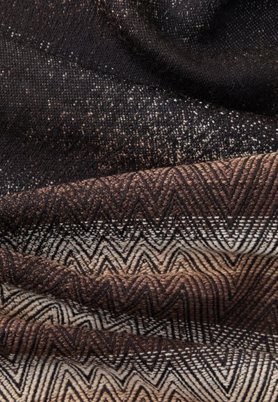 Strikket tekstil med et zigzag-mønster i nuancer af sort, brun og creme, med en tekstureret overflade og subtile metalliske fnug.