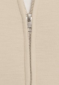 Beige gestrickter Zip-Hoodie mit einem silbernen Reißverschluss, strukturiertem Stoff und einem hohen Kragen. Der Reißverschluss befindet sich zentral.