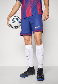 Tricou de fotbal cu dungi albastre și roșii, pantaloni scurți, ghete de fotbal negre, șosete albe și o minge de fotbal cu model și accente albastre.