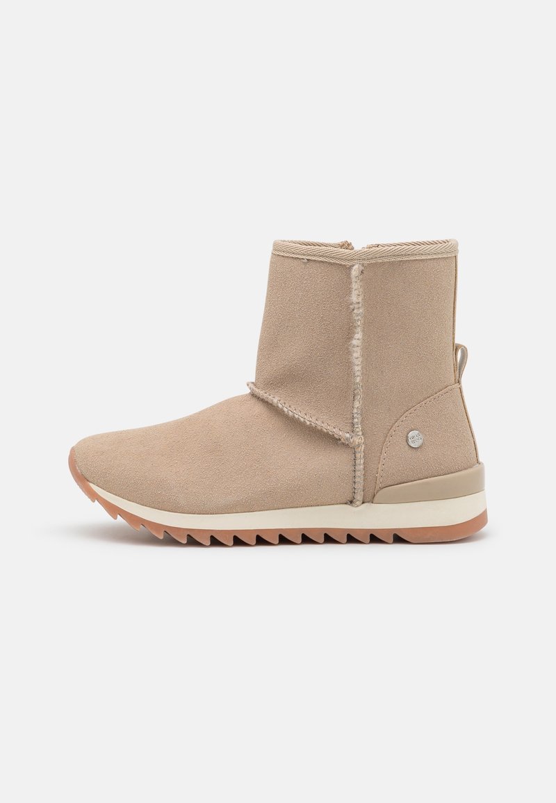 Botte cheville en daim beige avec doublure en fourrure, semelle en caoutchouc à motif en zigzag et petit logo en métal à l'arrière du talon.