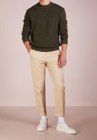 Mörkgrön stickad tröja, beiga byxor och vita sneakers. Tröjan har en rund halsringning och ribbade mudd och nederkant.