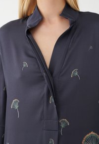 Blusa blu navy con colletto, caratterizzata da un design avvolgente e piccoli motivi floreali in verde e arancione. Tessuto morbido e leggero.