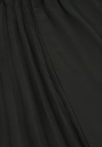 Tissu noir avec une texture douce, featuring des plis verticaux et des sections lisses. Le matériau semble léger et fluide.