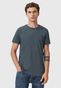 Camiseta corta de manga en gris oscuro, hecha de algodón, con cuello redondo y un pequeño logotipo bordado en el lado izquierdo del pecho.