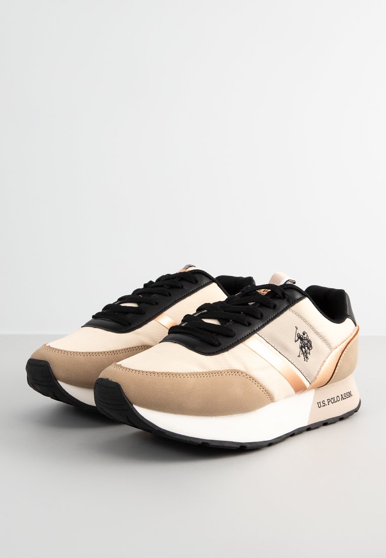 Zapatillas beige y negras con materiales de satén y ante, con una franja metálica, cordones negros y un logotipo en el lateral. Suela de goma.