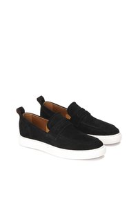 Zapatos sin cordones de ante negro con suelas de goma blancas, con un diseño cosido y un panel decorativo en la parte superior. Forro interior marrón y lengüeta en el talón.