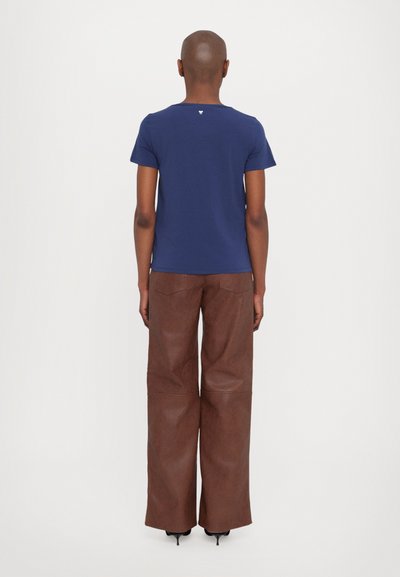 Σκούρο μπλε κοντομάνικο μπλουζάκι με στρογγυλή λαιμόκοψη και μικρή λογότυπη λεπτομέρεια στην πλάτη, συνδυασμένο με φαρδιά παντελόνια από καφέ ψεύτικο δέρμα.