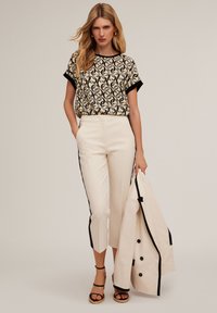 Krämfärgade och svarta mönstrade kortärmade topp med rund halsringning, tillsammans med krämfärgade capribyxor med svarta sidostråkar.