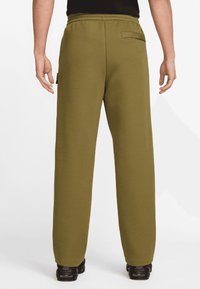 Olivgröna mjukisbyxor med avslappnad passform, utrustade med midjeband och en bakficka. Mjukt tyg med enkel design.