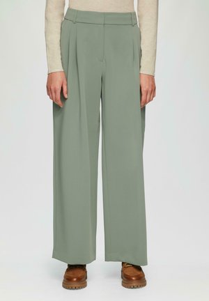 Pantalons à jambes larges en tissu vert doux, avec des plis à l'avant, une taille haute et des poches latérales. Associés à des chaussures à lacets marron.
