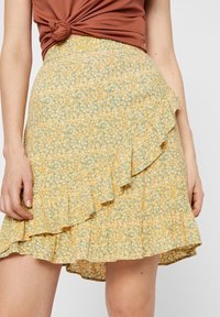 Květinová sukně do áčka v žluté a zelené barvě s volánkovým lemem. Lehká tkanina obsahuje malý květinový vzor; pas je přiléhavý.