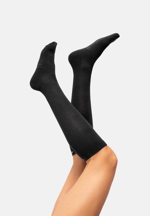 Knähöga svarta kompressionsstrumpor gjorda av texturerat material med ribbat mönster; har en logotyp på toppen och förstärkt tåområde.