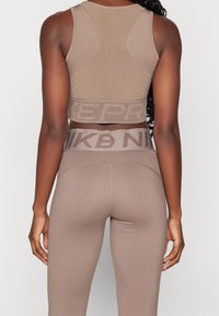 Top corto atletico marrone con schiena testurizzata e banda con logo. Leggings marroni a vita alta con fascia in coordinato con logo. Design morbido e aderente.