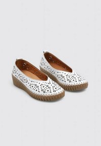 Zapatos slip-on perforados blancos con punta redondeada, suela de goma beige y tacón cuña texturizado. El interior cuenta con un forro marrón suave.