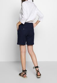 Marina blå shorts i bomull med rullad fåll, med bakfickor och knappdetalj. Matchat med en vit tröja med trekvartsärmar.