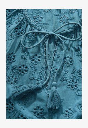 Hele sinine tikitud pluus, millel on lillemustrid, seotav detail ja pitsid. Pehme kangas tekstuursete õmbluste ja välja lõigatud aktsentidega.