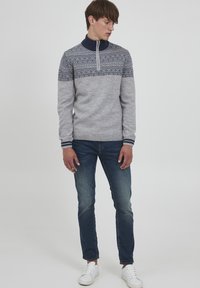 Lys grå strikkegenser med en marineblå høy krage og mønstredd bærestykke. Kombinert med mørkeblå jeans og hvite joggesko.