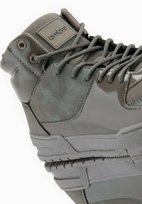 Zapatillas altas en tonos gris apagado. Presentan una superficie texturizada con acentos suaves, suela de goma y ojales reforzados para los cordones.