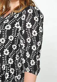 Robe noire avec un motif floral blanc, manches courtes bouffantes et taille froncée, confectionnée dans un tissu léger.