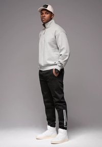 Szara bluza z zamkiem, czarne zwężane dresy w białe paski oraz białe trampki za kostkę. Dodatki to lekka czapka i zegarek.