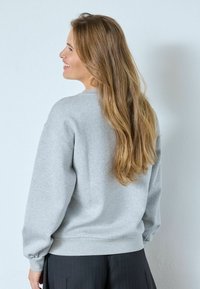 Szürke pulóver puha anyagból, kerek nyakkivágással és bordázott mandzsettákkal, laza szabással és minimális varrással.