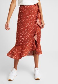 Gonna a portafoglio color ruggine con pois bianchi, realizzata in tessuto leggero, con orlo arricciato e fiocco laterale.