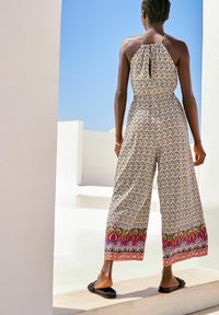 Combinaison à motifs multicolores avec un décolleté halter, des jambes larges et une bordure décorative à l'ourlet. Portée avec des sandales plates noires.